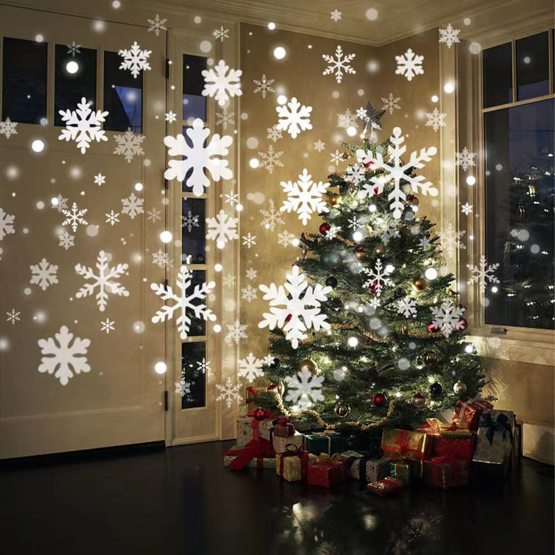 Snowfall laser light effect projected on a wall next to a Christmas tree at night